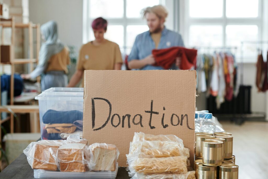 pexels-photo-6994982-6994982 Volunteers sort clothes and food in a donation center. Cardboard sign reads 'Donation.'